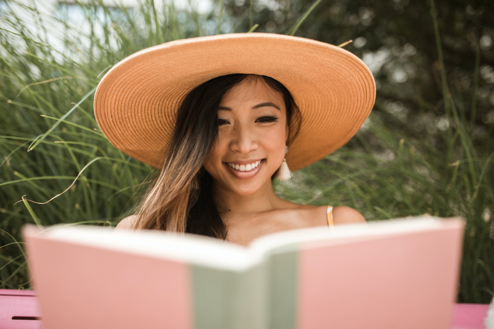 smiling woman wearing a sun hat and reading a book